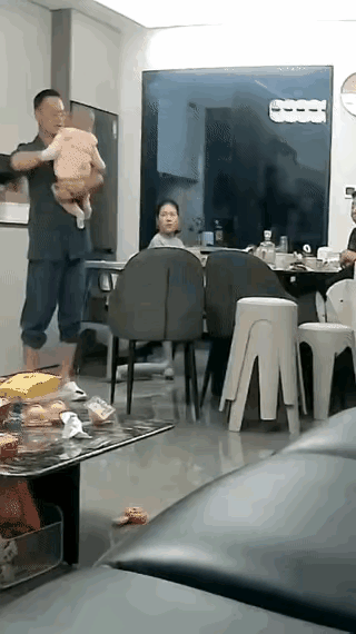 这真是一个不合格的父亲。妻子与婆婆正在餐桌上吃饭，丈夫则抱着小孩，一边抱一边哄。