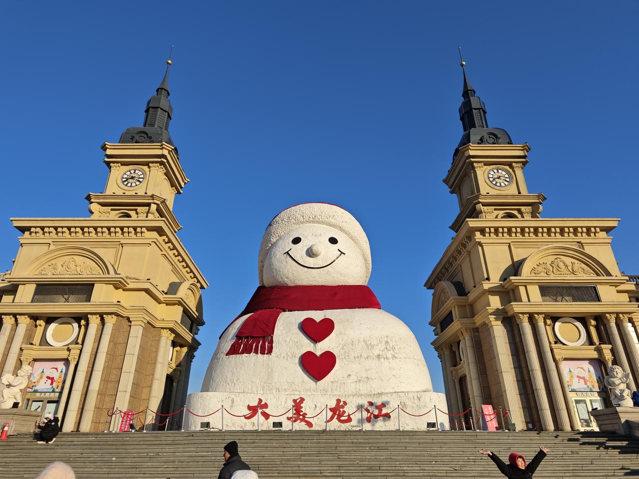 分享一张最近随手拍的照片在哈尔滨的冬日暖阳里，巨型雪人裹着红围巾站在欧式建筑前，