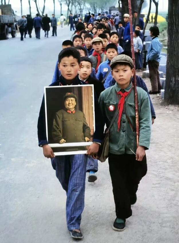 老照片里，一群乡村少年正列队走在林荫道上。最前方的孩子小心翼翼捧着毛主席的画像，