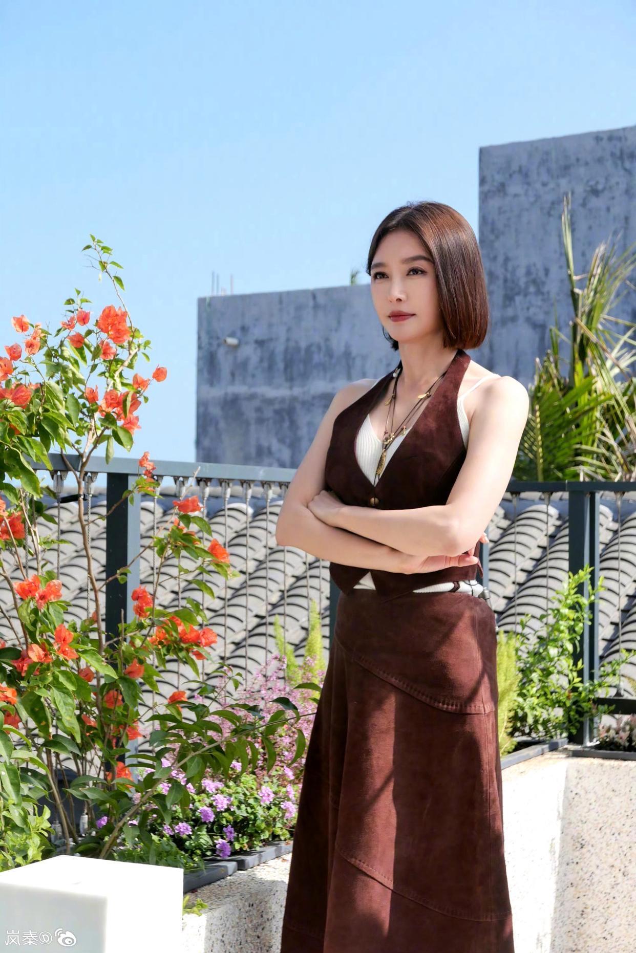 秦岚这组天台随拍，把「自在从容」写在了每一个细节里。
深棕麂皮挂脖马甲叠穿白吊带