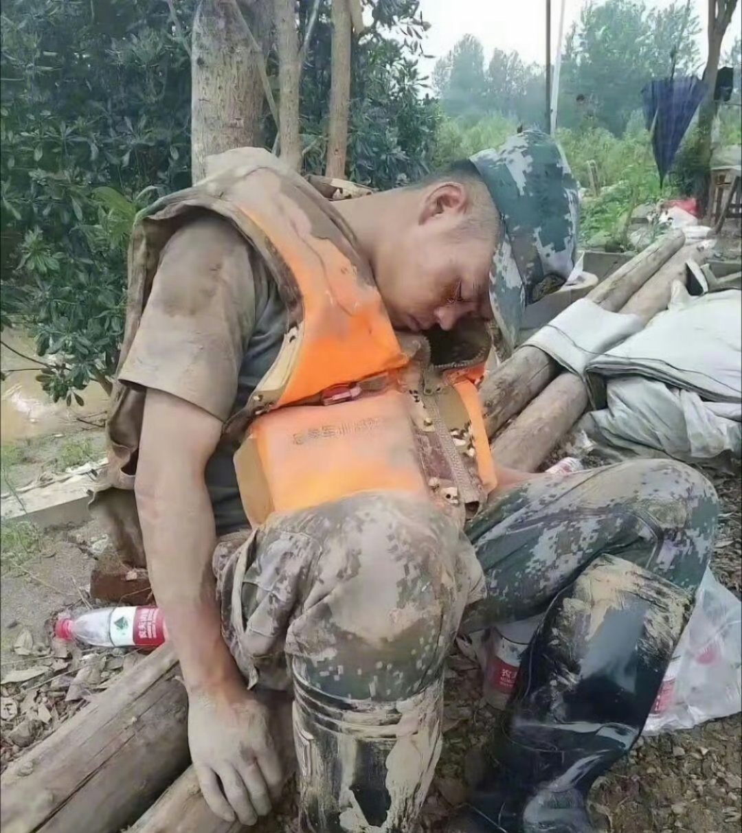 刷到这张照片真的破防了——一个浑身泥浆的兵哥哥，靠树睡着了，橙色救生衣都没脱。又