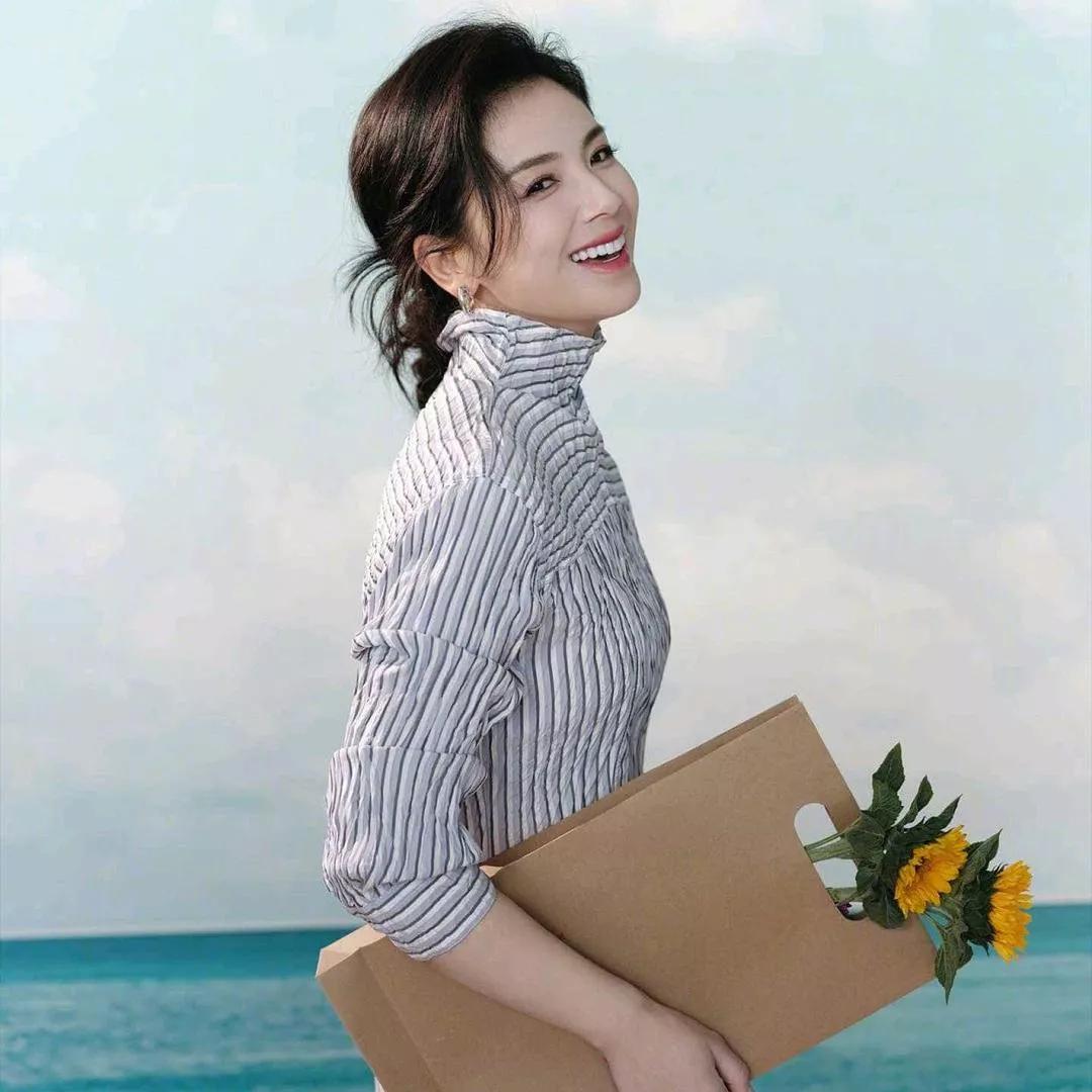 阳光沙滩上的快乐女孩，手捧鲜花，心旷神怡。海边花海少女 海边度假少女 海边微笑美