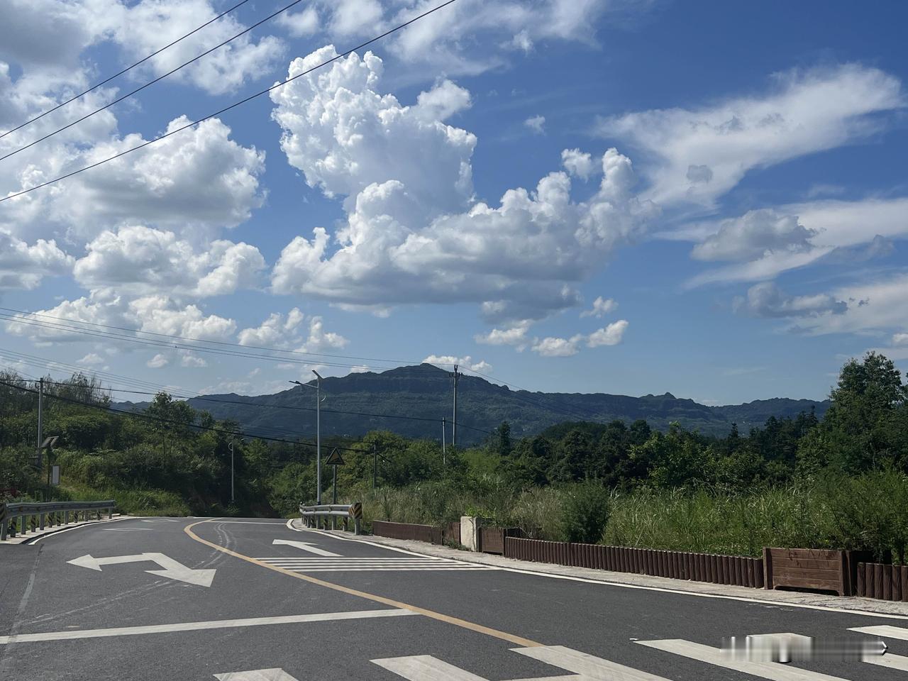 拍一张漂亮的天空图蜿蜒的柏油路在青山间延展，白色箭头指明方向。路旁木栅栏与绿树相