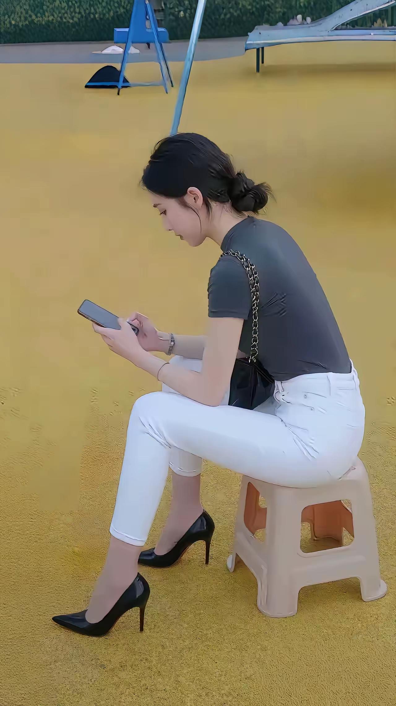 一个姑娘坐在小凳子上玩手机。