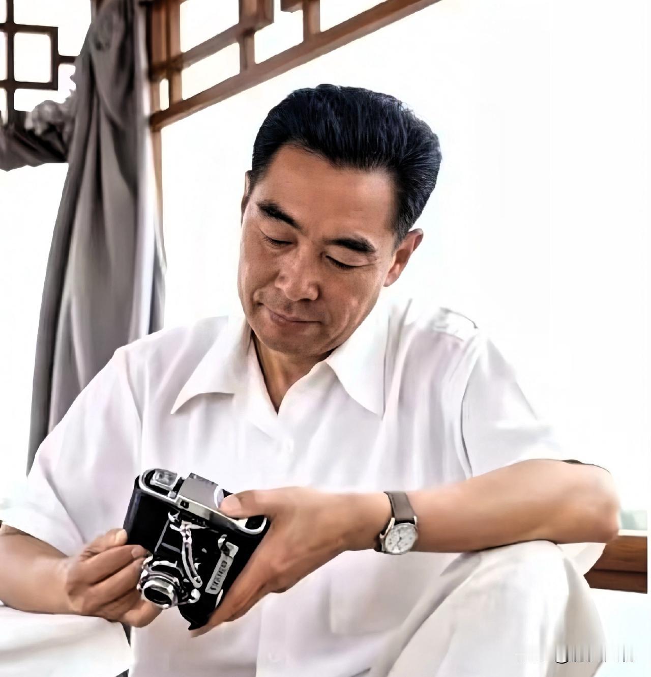 大概是1960年代，身着素净白衬衣的周恩来总理，凝神端详手中相机，神情专注平和，