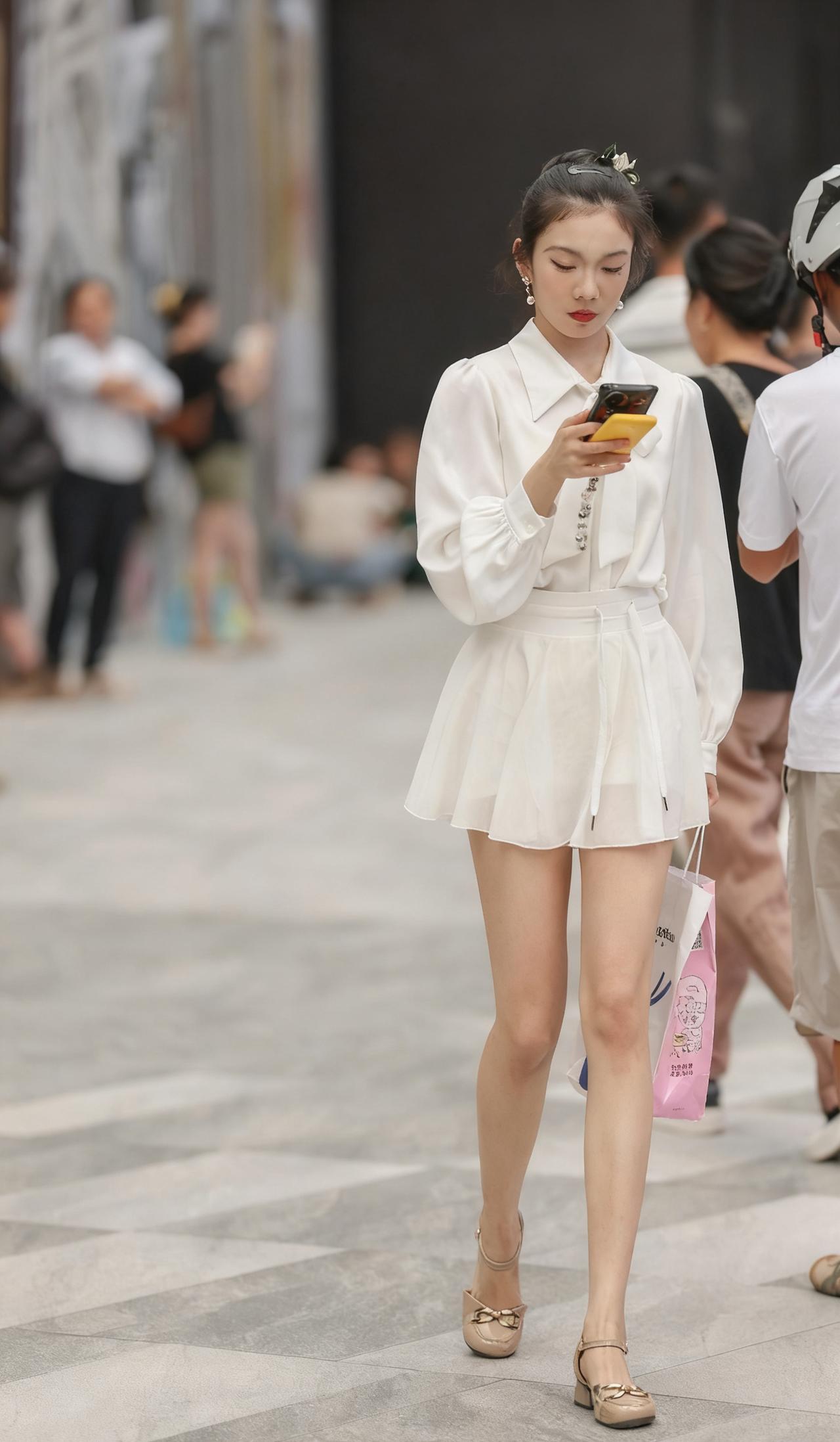 都市时尚女孩，白色连衣裙搭配高跟鞋，手拿手机和购物袋，漫步街头。