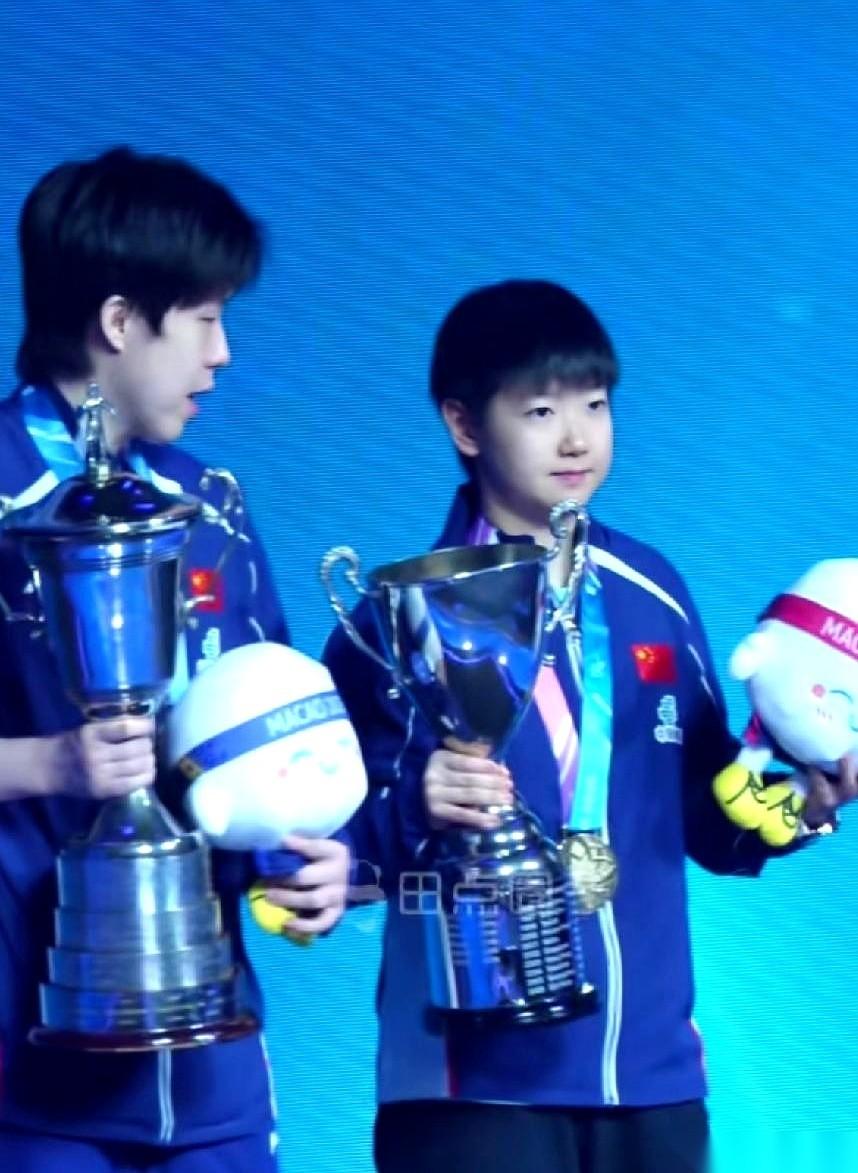 澳门世界杯冠军合影现场，闪光灯亮成一片。
王楚钦，第一次捧起这个沉甸甸的奖杯，手