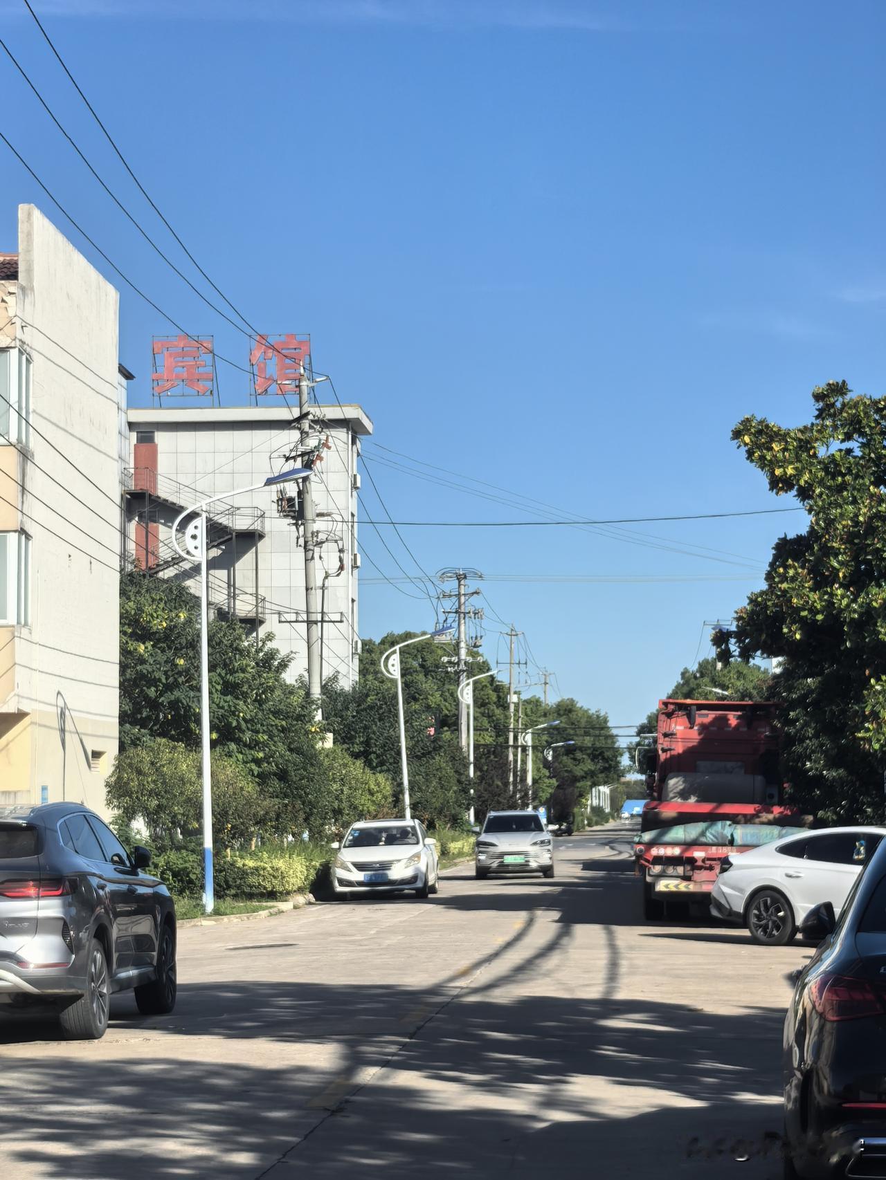 各色车辆往来穿行，远处楼宇顶的红色“宾馆”招牌，在晴空下格外显眼。路灯、电线顺着