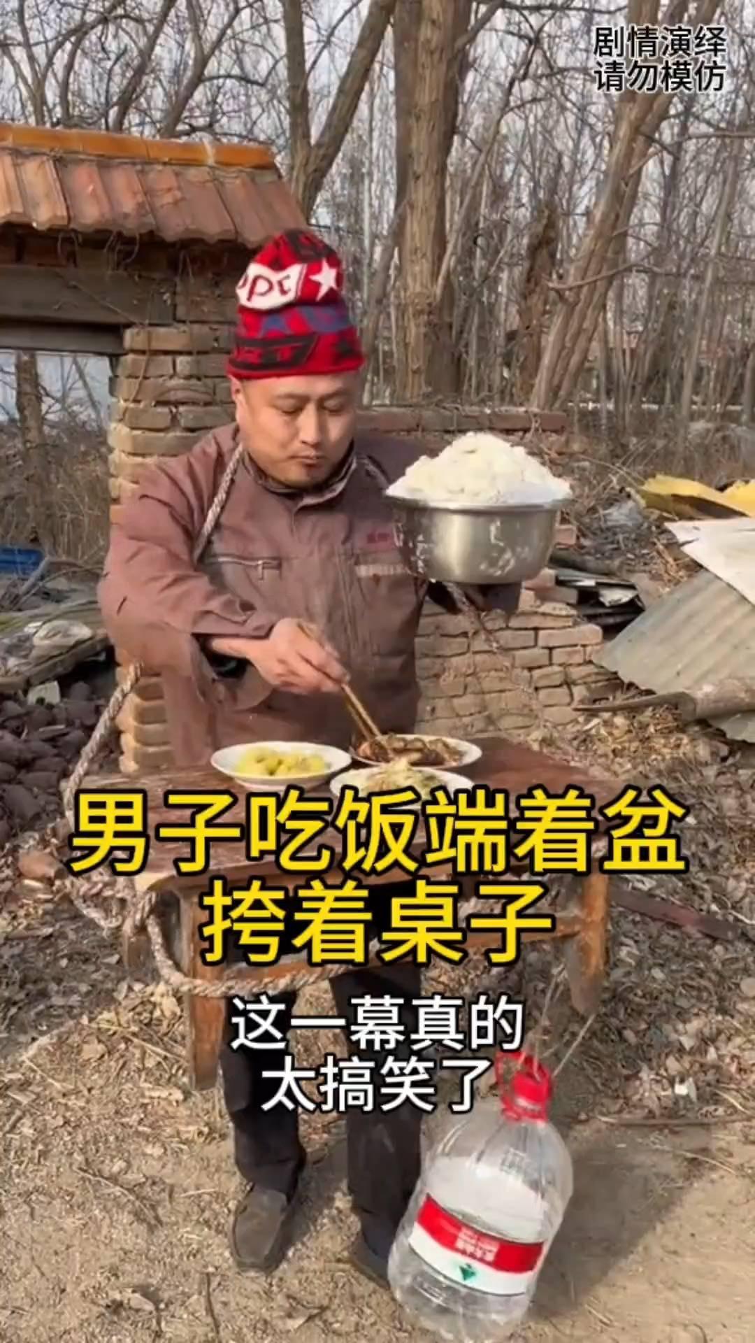 男子吃饭端着盆挎着桌子。
男子吃饭不想在家呆，于是他挎着桌子出去吃饭。只见桌上摆