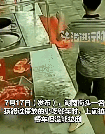 一名男孩在湖南的某个街道走着，看到旁边有个无人看管的小吃餐车，伸出他那双小手拽了