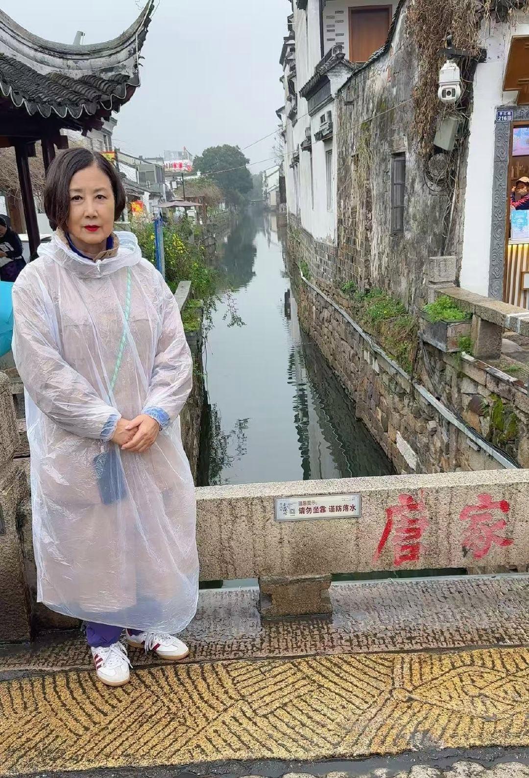 汪明荃现身苏州，穿着雨衣探古镇，展现别样风情。不得不说，汪明荃的这个雨衣造型，与