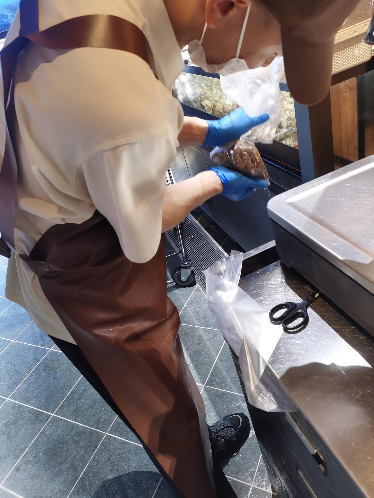双手接过塑料袋，拿起工作台上的剪刀，“咔嚓”一下，给塑料袋下面一个角剪个小口，然