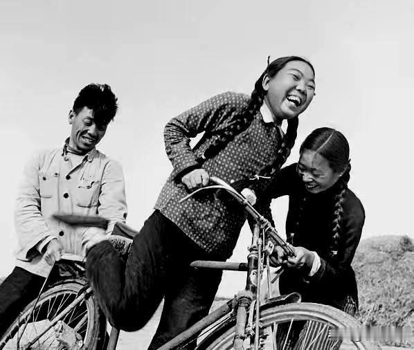 上世纪五十年代的乡村，田间的空地上，姑娘正学着骑自行车，身旁同伴帮忙扶稳车把，一