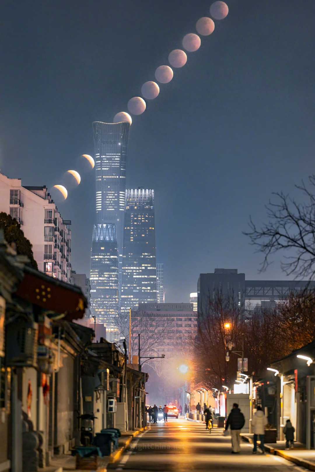 旧城的灯暖，高楼的光冷，月亮在两者之间悄悄画出一道弧线，由盈转亏，由白转红——那