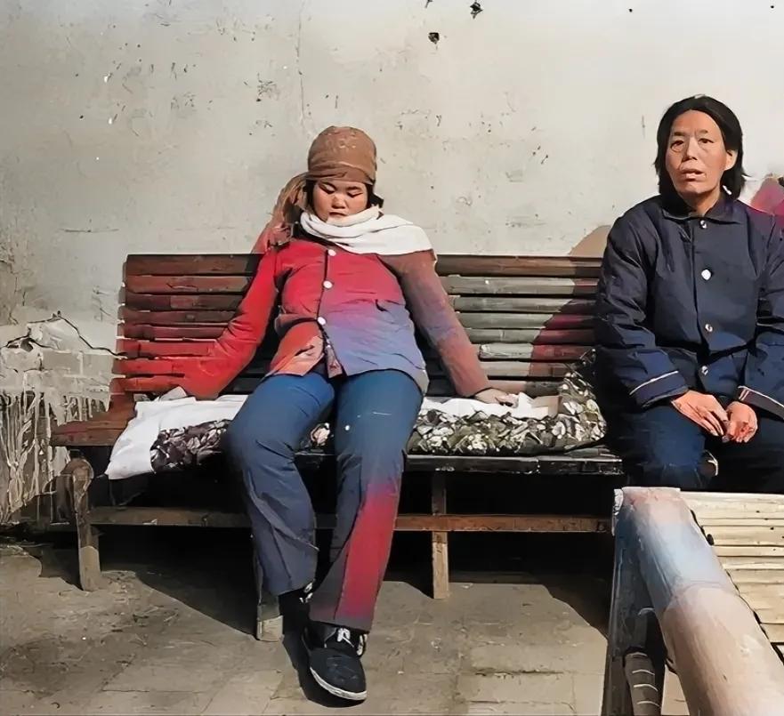90年代初，一名即将做“结扎手术”的妇女，坐在长凳上，看起来面露不悦，旁边的人是