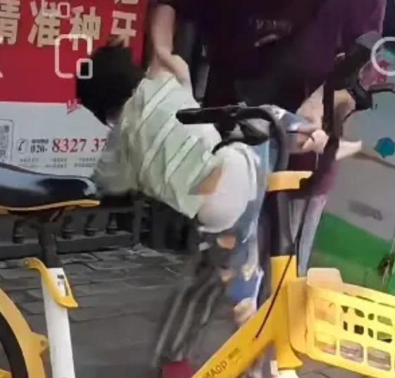 广州荔湾，一女子当街拎起男童的一只手和一条腿，像丢物件一样把他塞进路边的共享单车