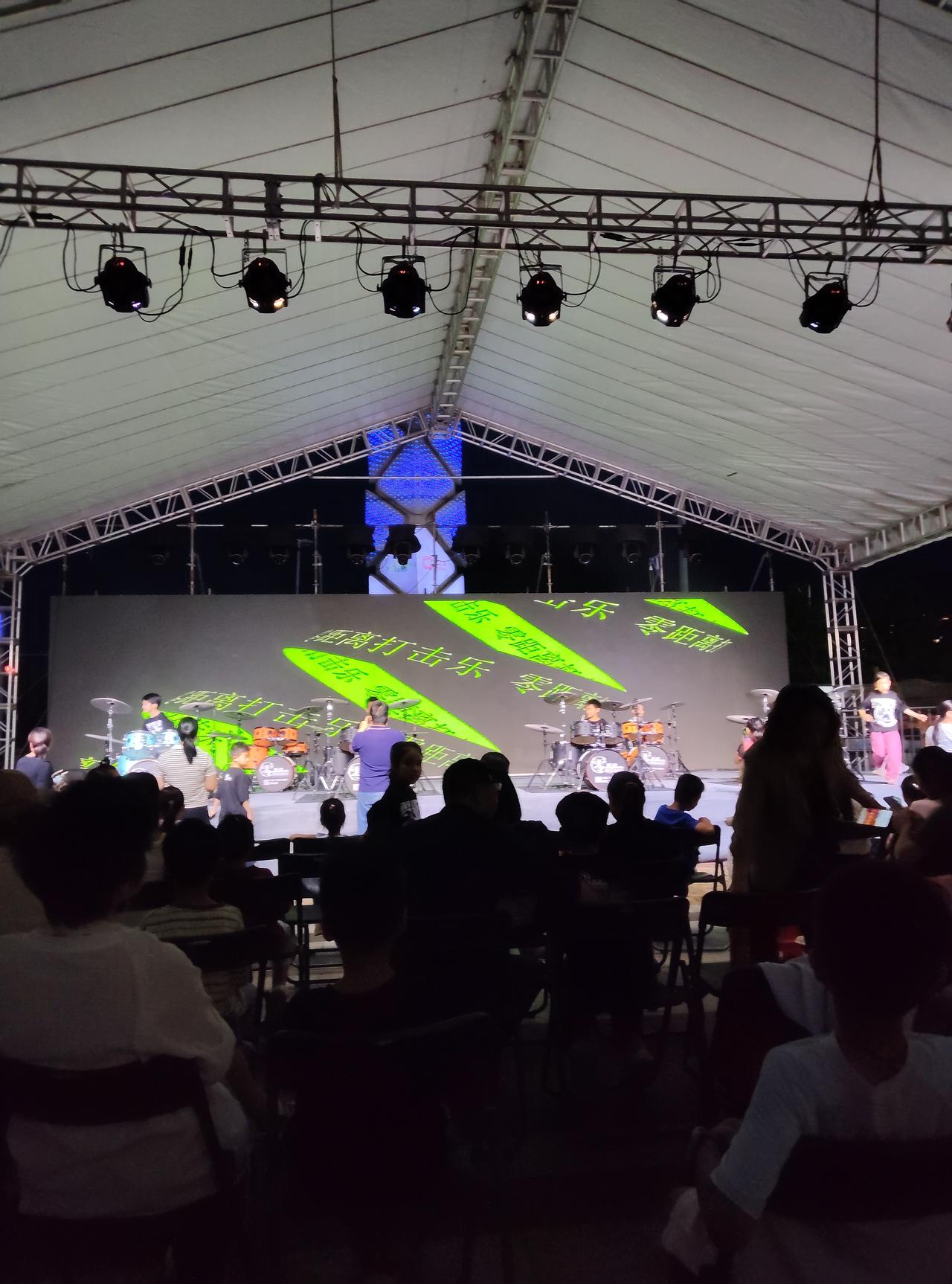 今晚来到户外架子鼓演出现场，现场气氛特别热闹。夜幕慢慢降临，舞台灯光亮起，小小的