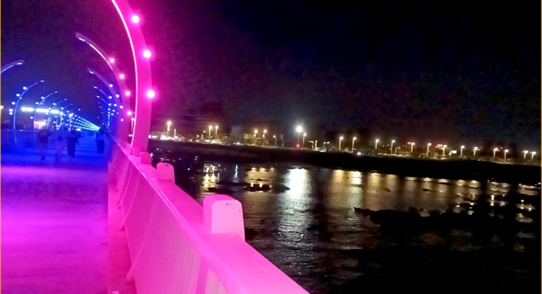 彩光漫过栈桥，灯火坠入海面。晚风拂过夜色，粼粼波光伴着流光，把海边的夜晚揉成温柔