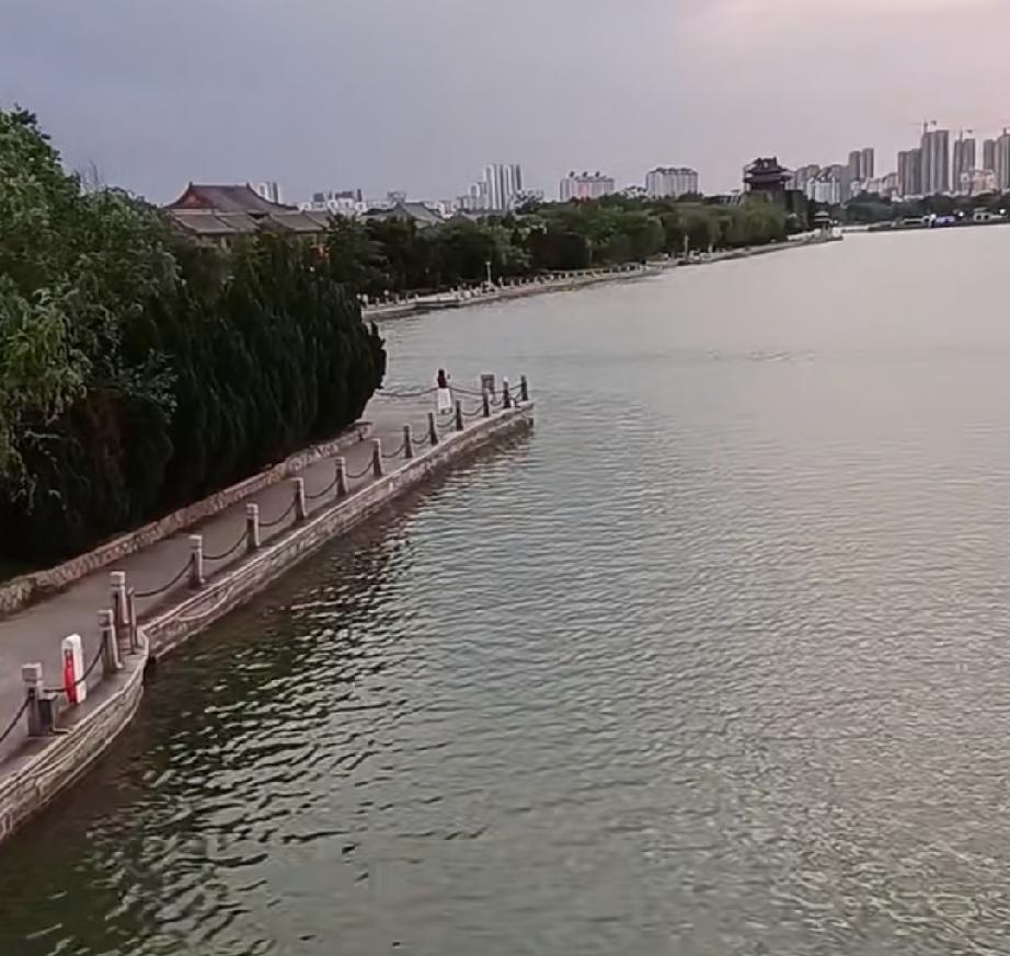聊城东昌湖风景区的北关桥一带，湖面映着晚霞，水天相接宛如幻境，岸边绿树成荫，远处