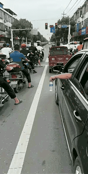 路口等候红绿灯的一幕，反差感实在太过扎心。小轿车车主随手将矿泉水瓶丢在马路中央，