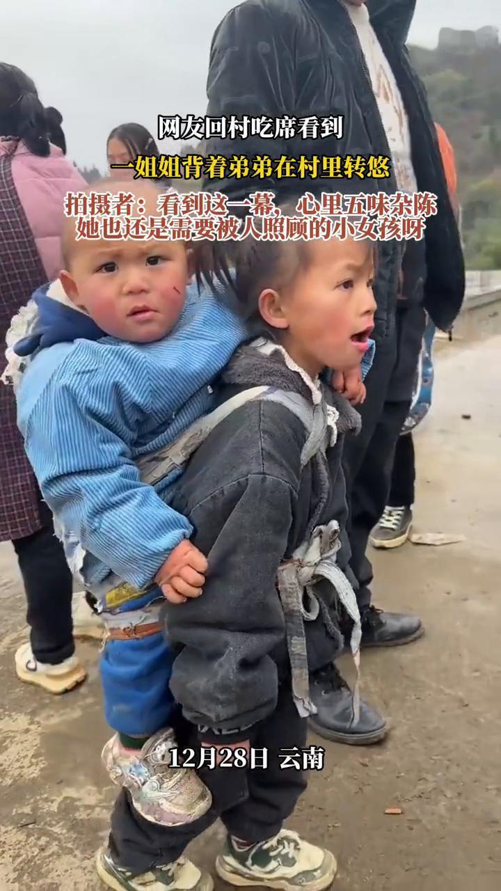 网友回村吃席看到一姐姐背着弟弟在村里转悠。拍摄者：看到这一幕，心里五味杂陈。
1