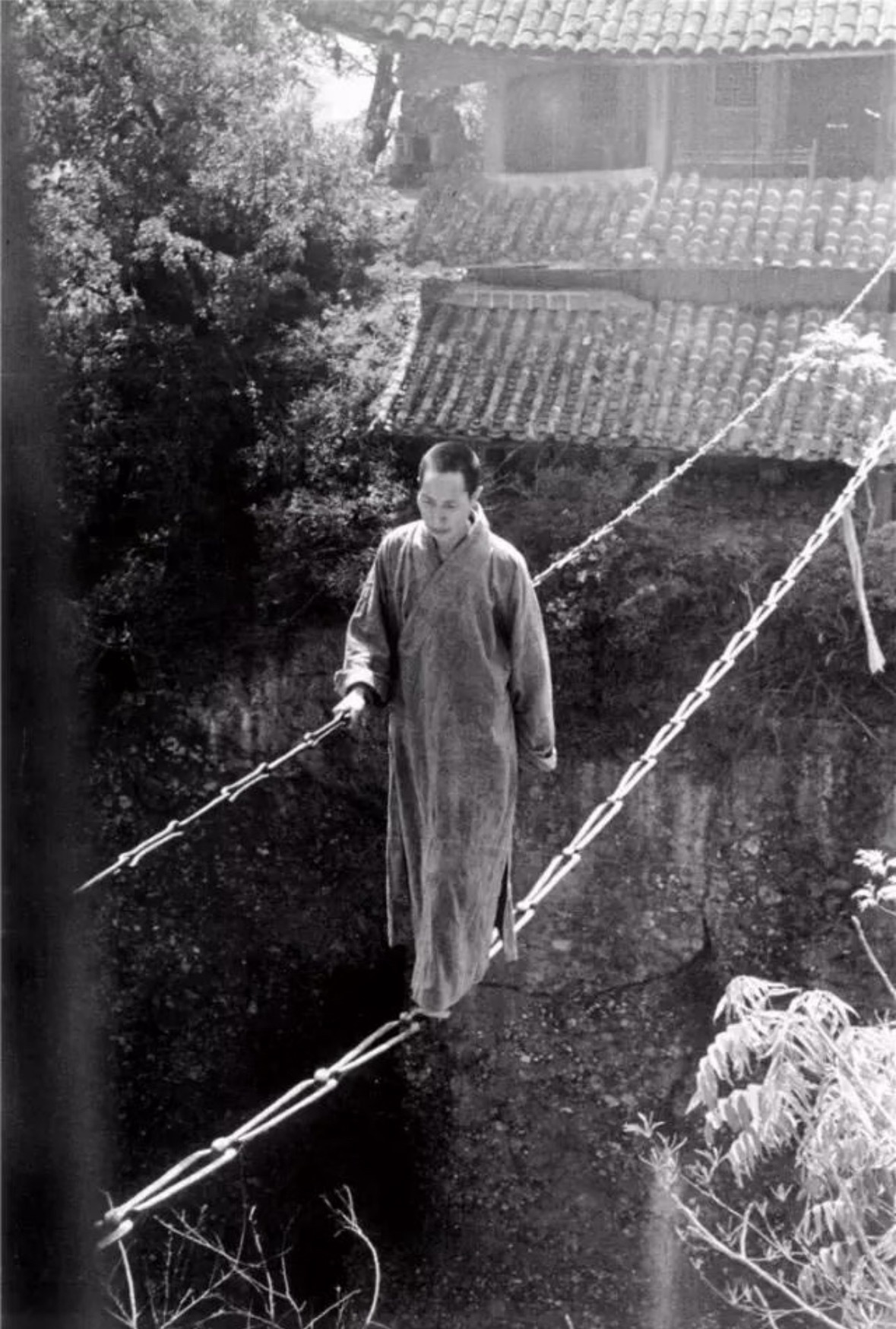 1930年代，在四川江油窦圌山上的寺庙里，一位出家人正踩着一根简陋的铁链子过悬崖