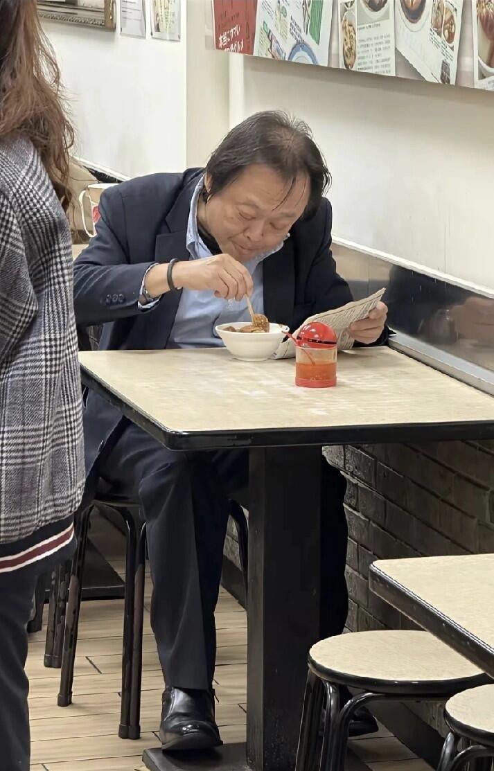 这是那个男明星，一个人安安静静坐在那里吃东西，他的头发稀疏，发际线后移，能认出他