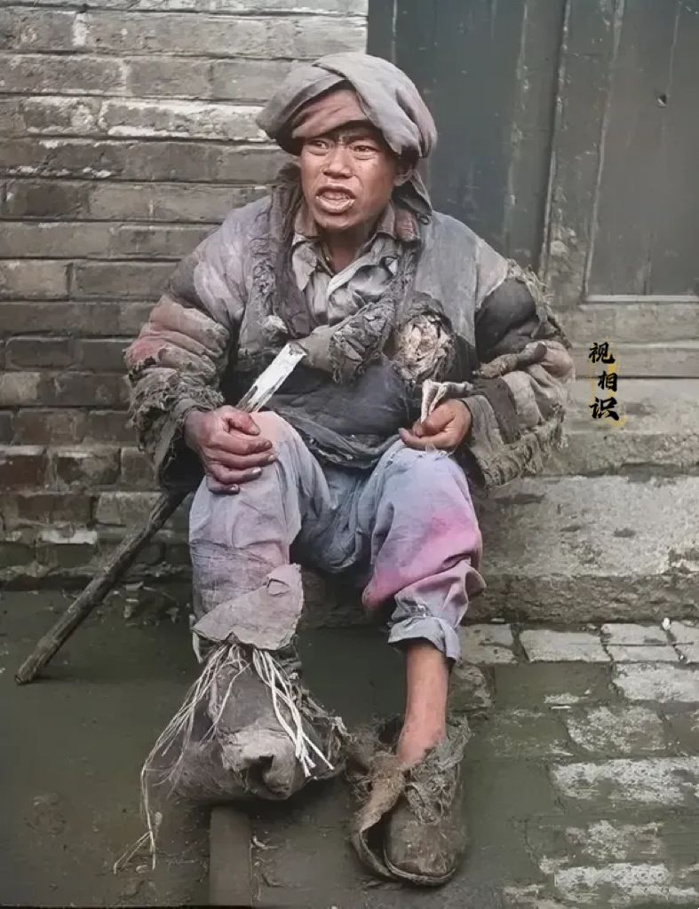 1920年，北平街头，一名乞丐坐在地上的照片，镜头中他衣衫褴褛，在寒风中冻得瑟瑟...