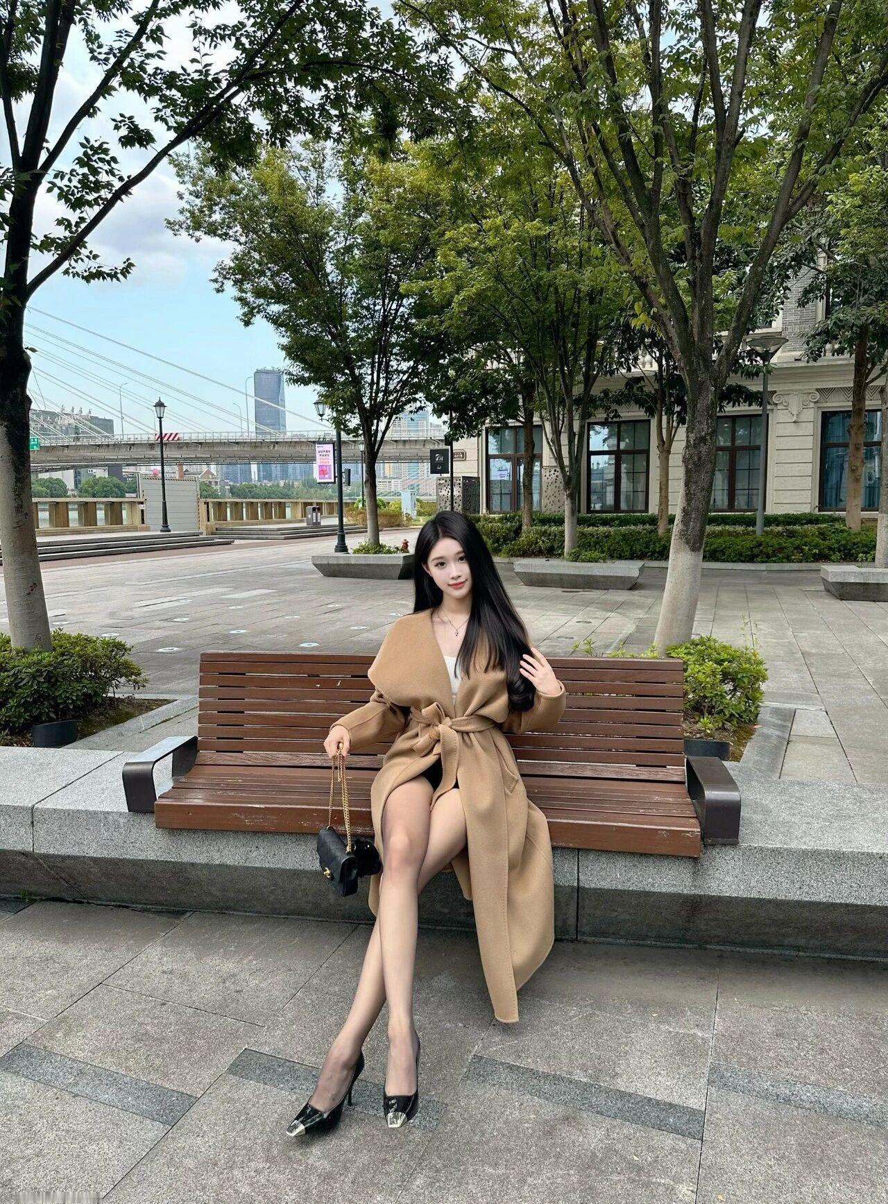 米色大衣的羊毛纤维在秋阳下泛着柔光，她坐在铸铁长椅上，像幅被精心装裱的油画。黑色