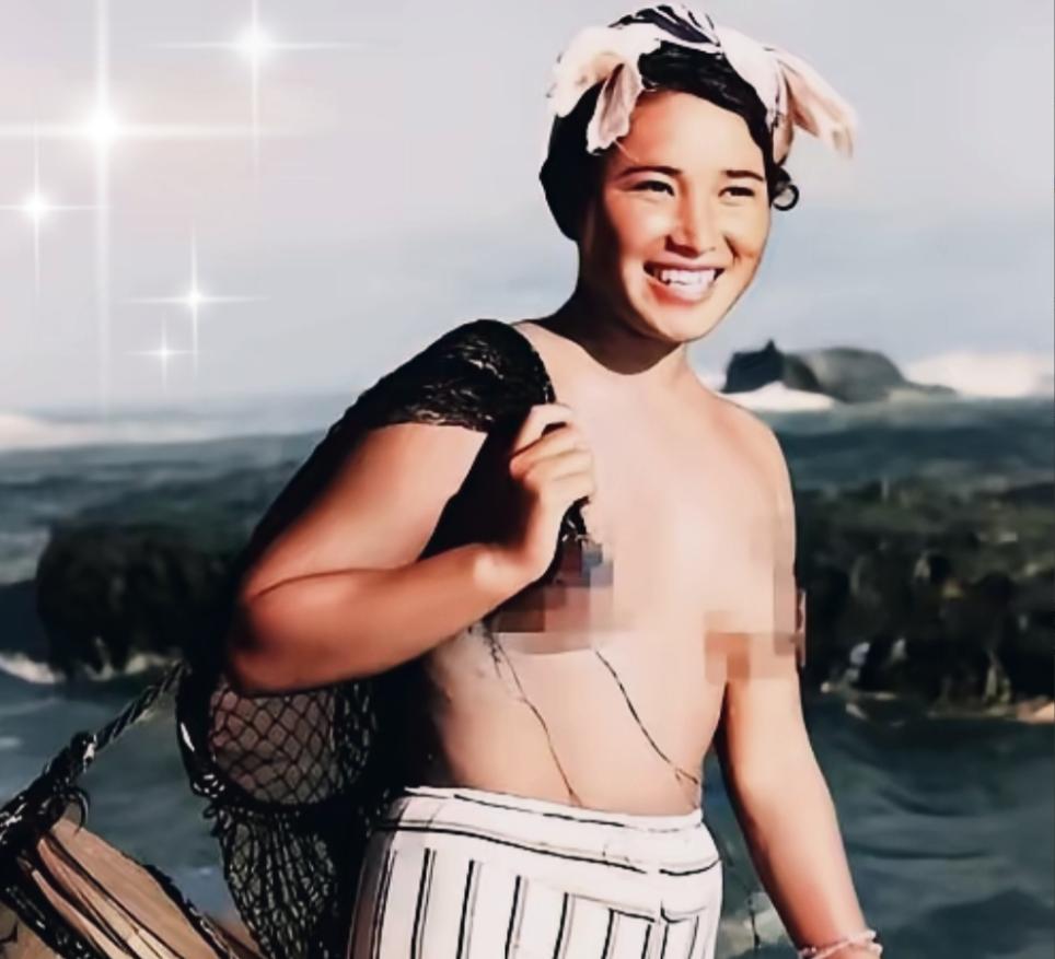 1955年，一名身体强壮的日本女人赤裸上半身，背着一个黑色的编织袋站在海边。这个