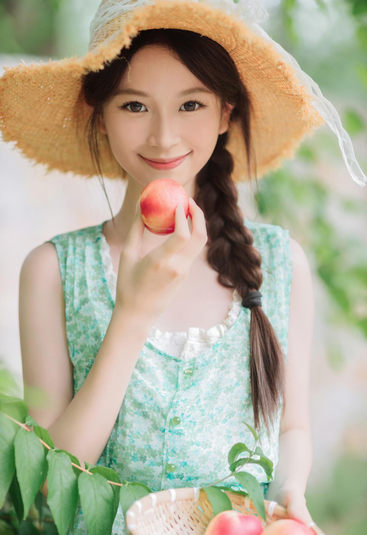 戴着宽檐草帽，穿着碎花绿裙，握着一颗饱满的红桃，像是握住了整个夏天的甜美。绿意环