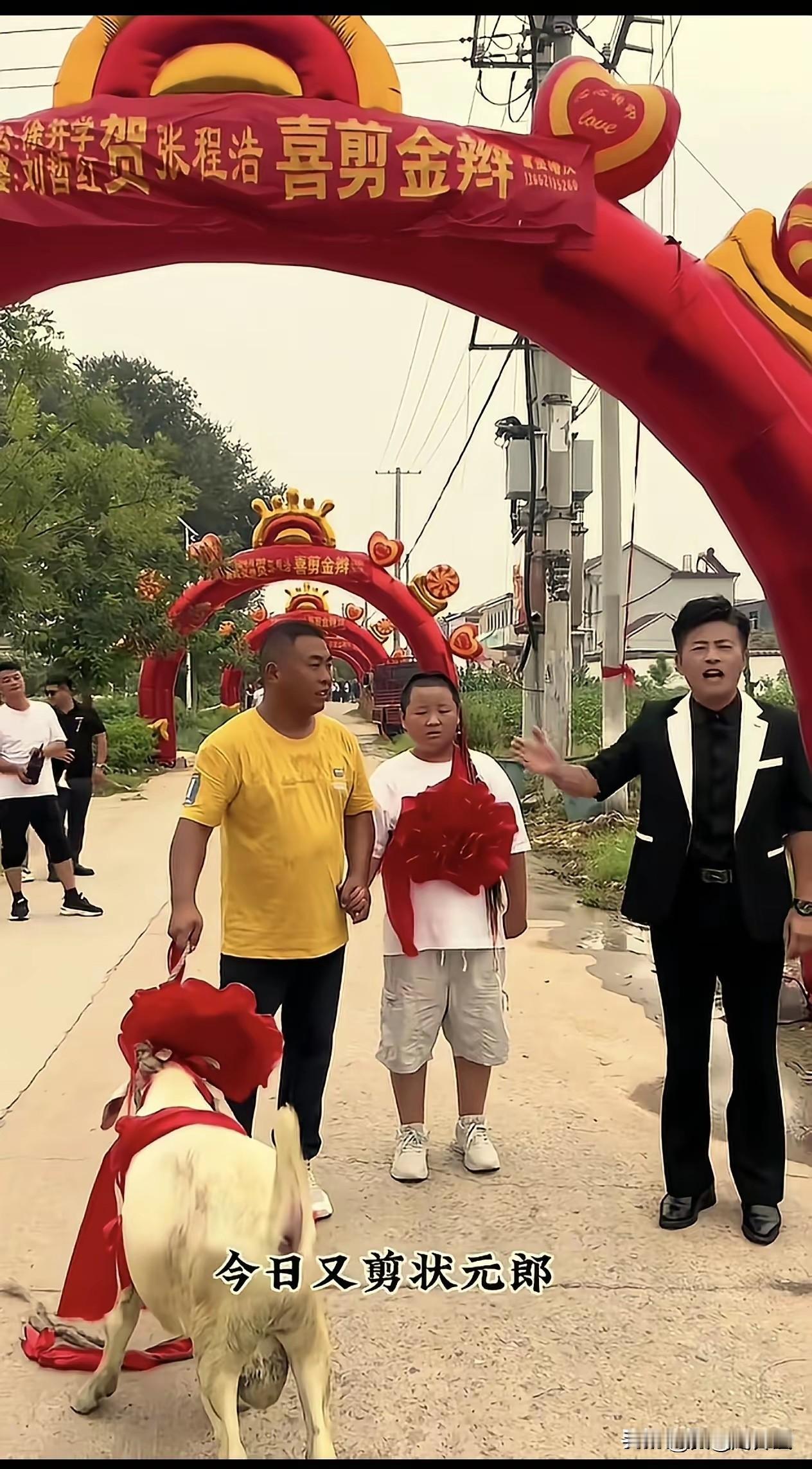 刷到这一段农村实拍画面，一排红彤彤的充气拱门绵延老远，孩子胸前佩戴大红花，现场热
