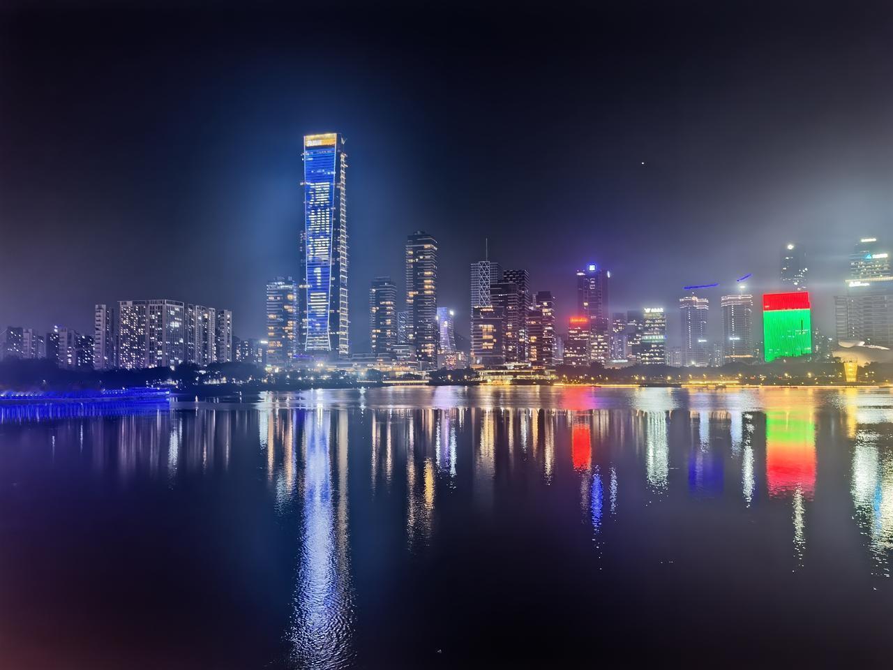 城市魅力夜景霓虹在高楼的骨节间流淌，将夜的静脉照得发亮。摩天楼群躬身探向水面，玻