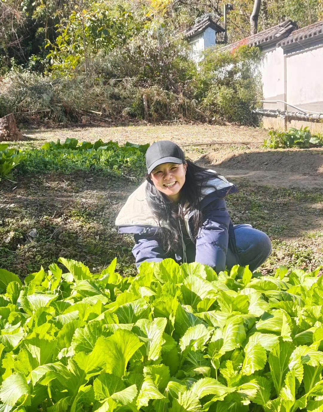 龚琳娜近照，
穿着厚厚的外套，
脸上露出灿烂的笑容，
摘菜的样子分明是普通老百姓