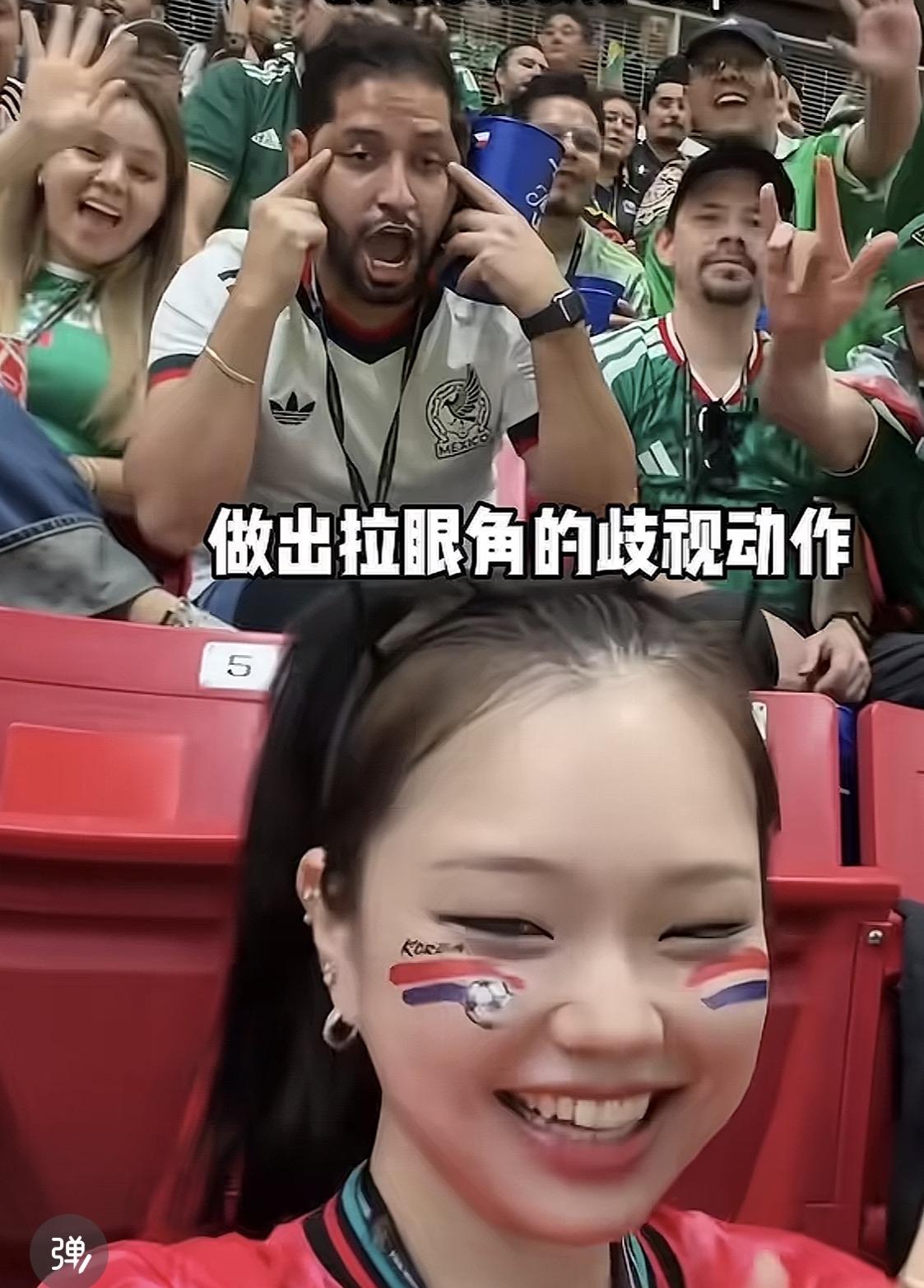 美加墨世界杯赛场，一韩国球迷看台上看球自拍，身后一个墨西哥人拉眼角作出歧视的动作