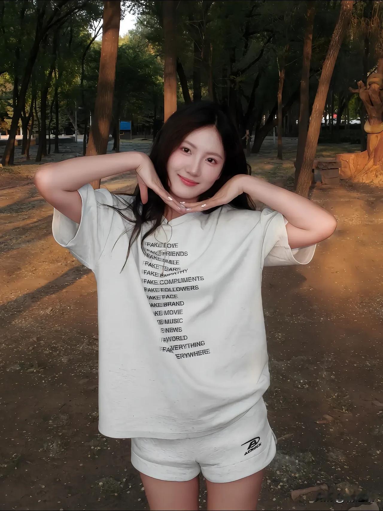在公园里，穿白色T恤的少女，微笑着比出爱心手势，阳光洒在身上，温暖而美好。