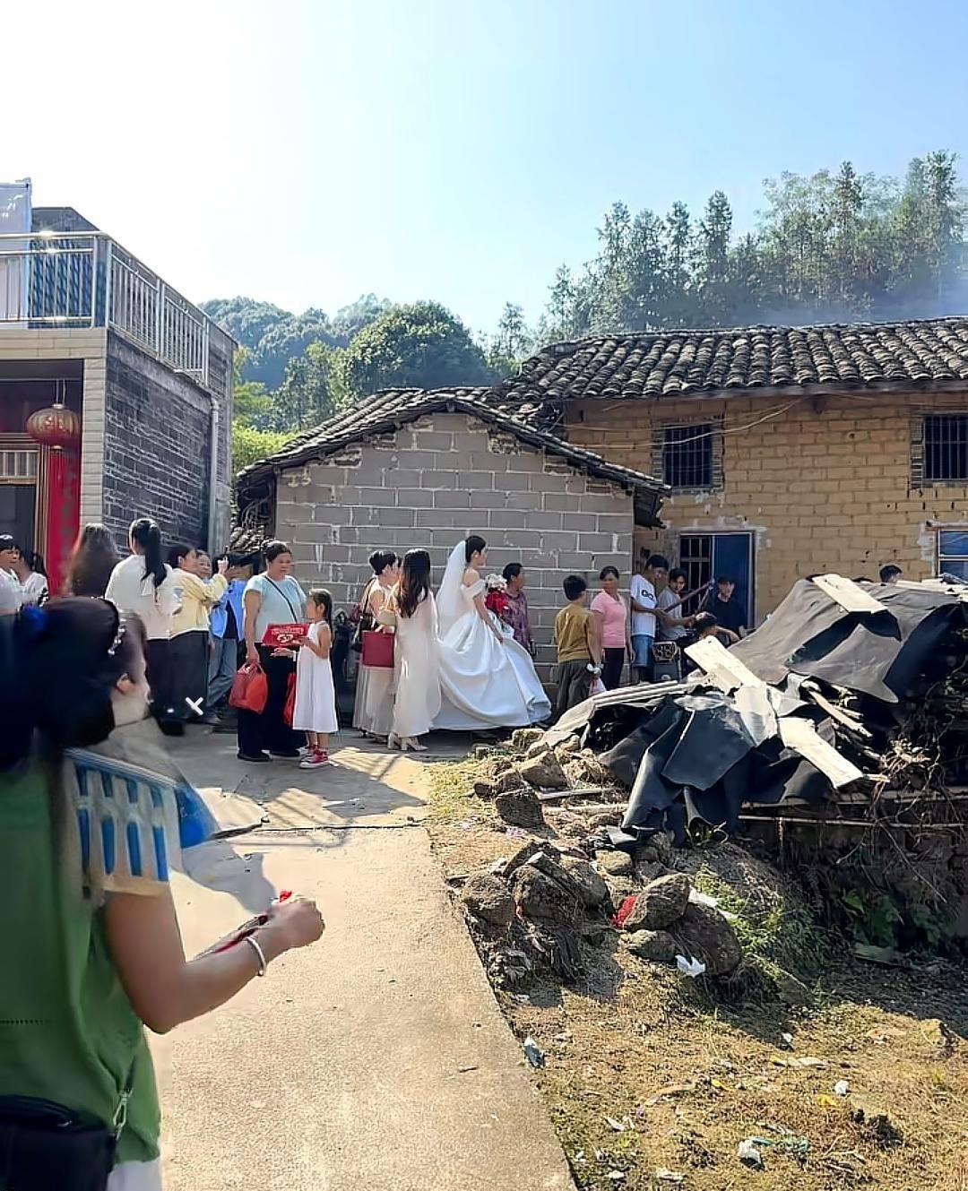 新娘一袭洁白婚纱，踩着乡间小路走向老旧土坯房，周边站满了看热闹的乡亲，不少人悄悄