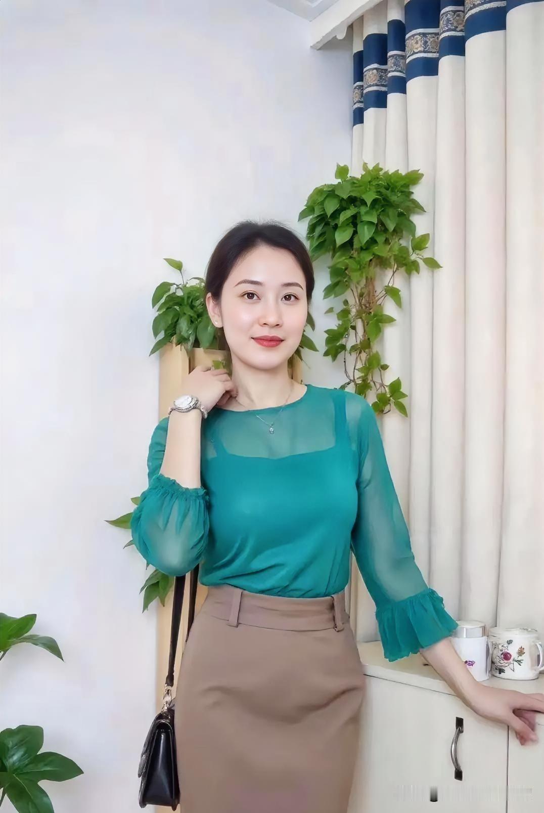 翠绿纱质上衣搭配卡其半裙，于室内绿植旁定格优雅，温婉知性尽显都市女性从容之美。