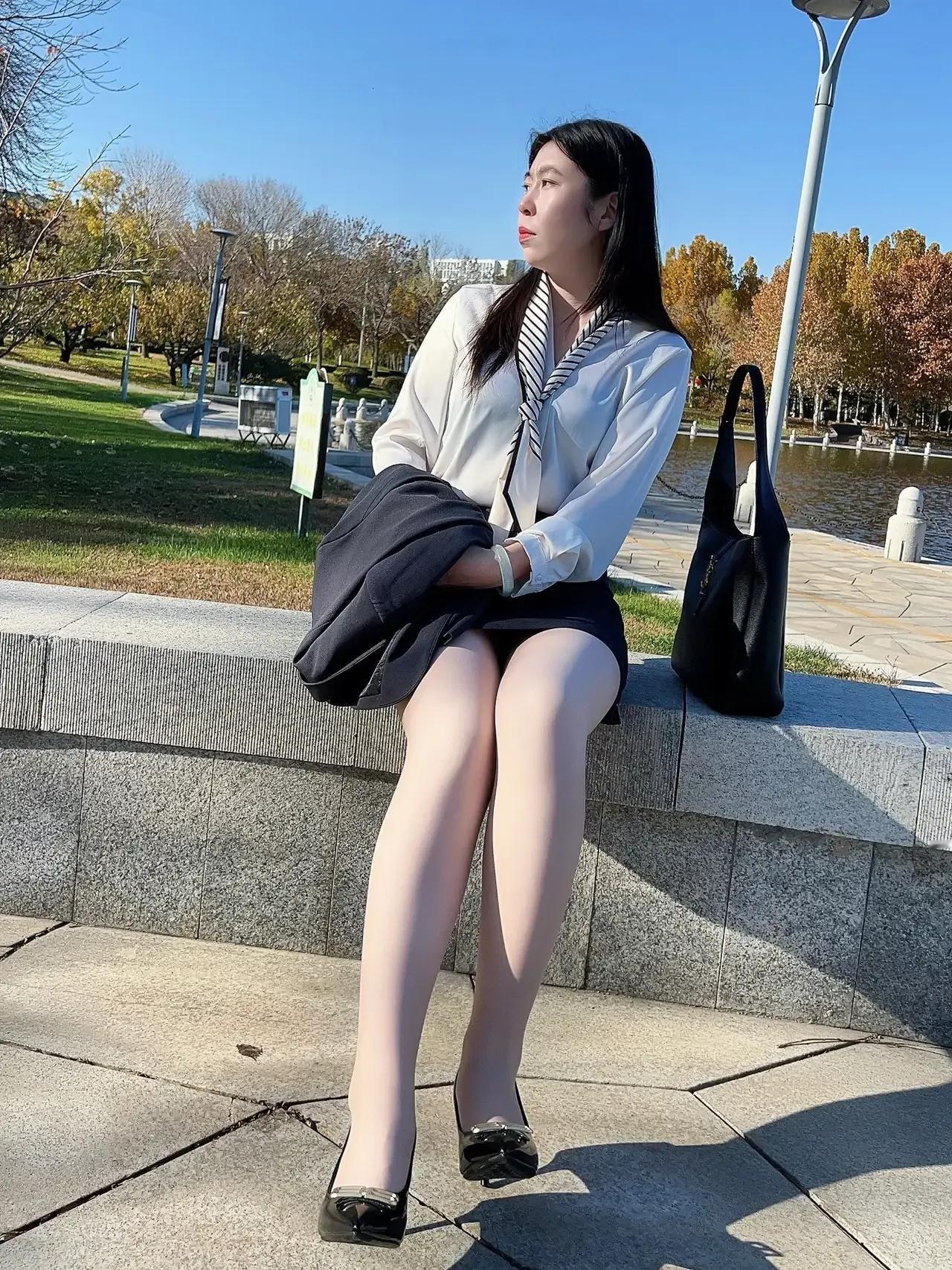 一个女孩坐在公园的石墙上，看着远方。