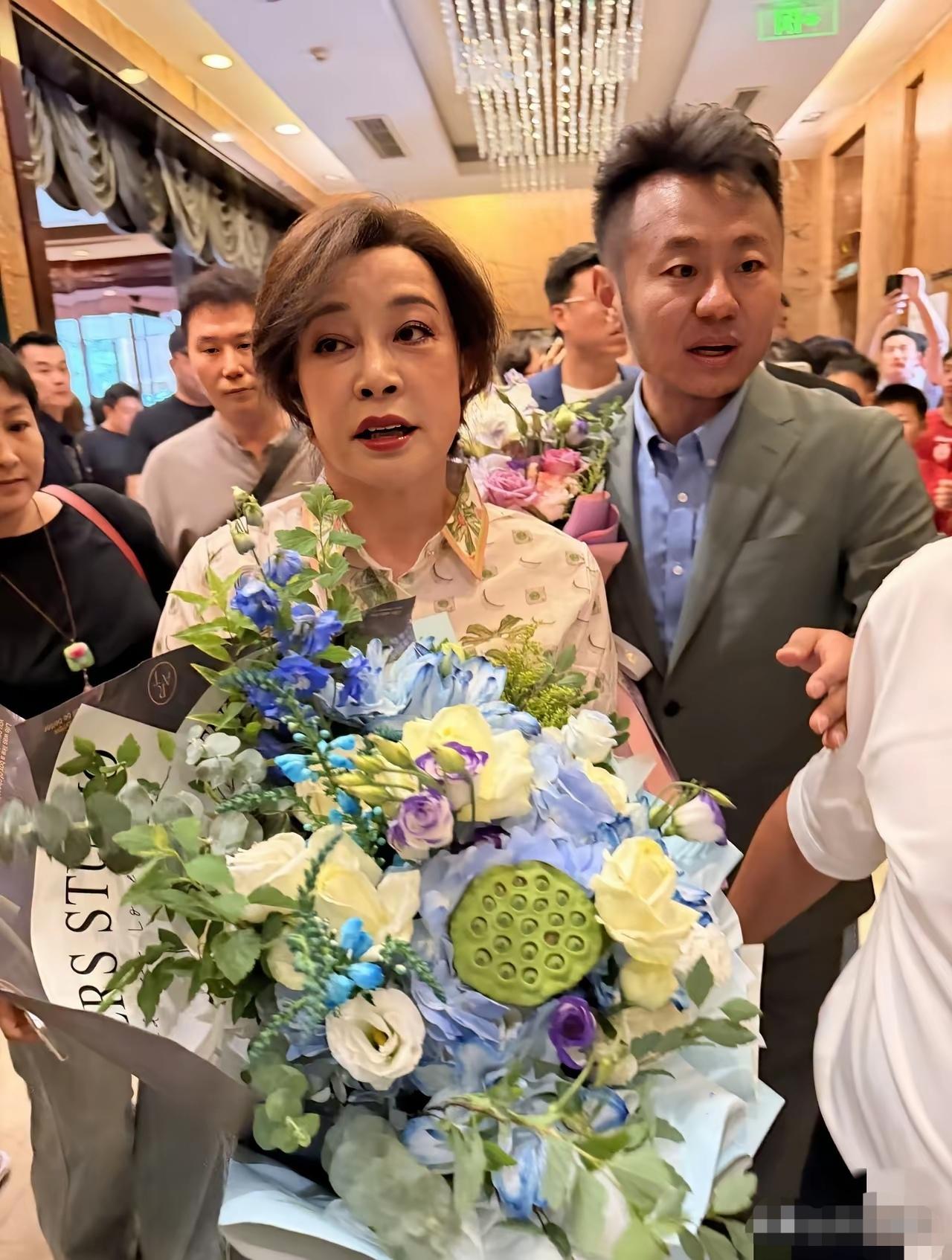 刘晓庆手捧鲜花在北京露面了，这次的穿着打扮非常素雅漂亮，妆容也很干净。比以往漂亮