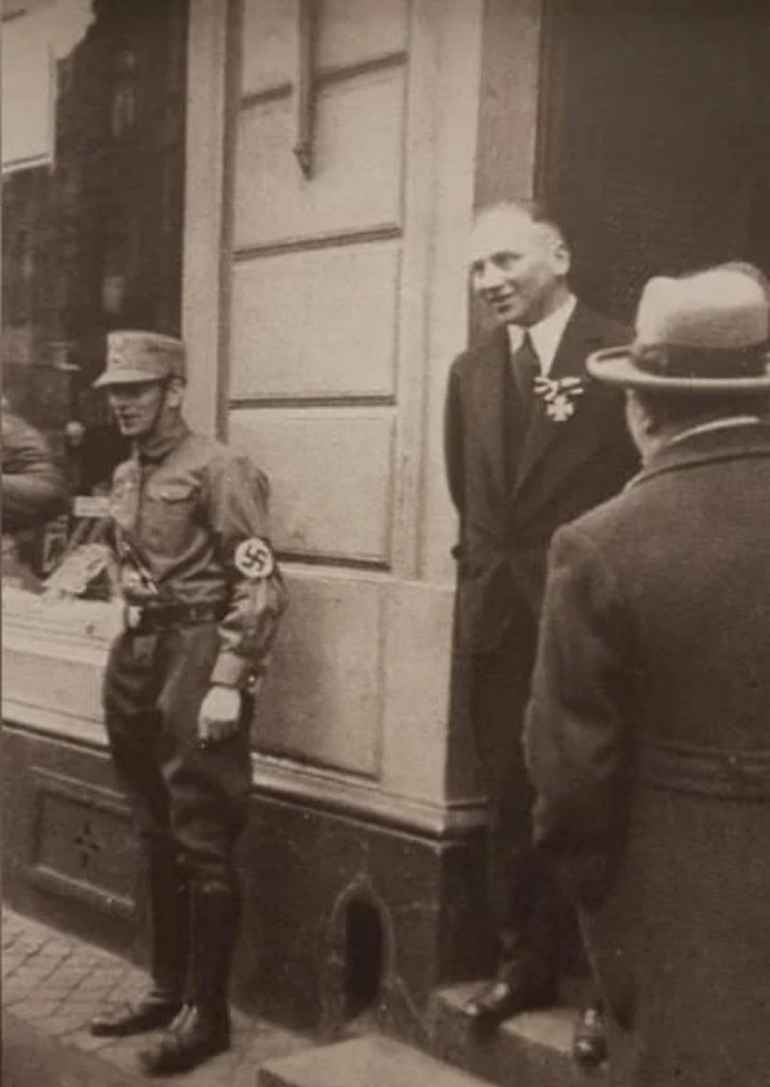1933年，一位德裔犹太人一战老兵佩戴着他的铁十字勋章站在自己的商店门口，而一名