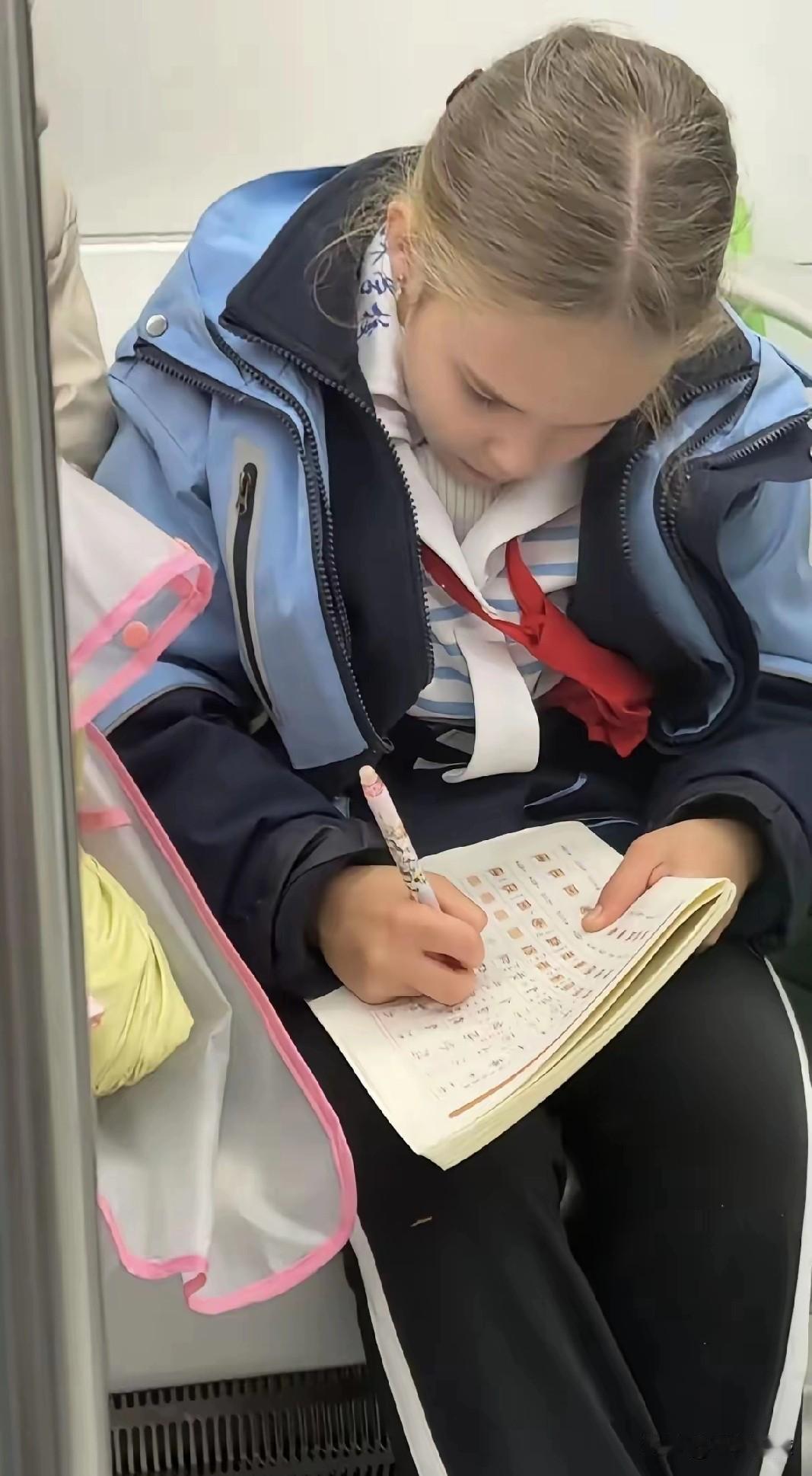 这个坐在地铁上的小朋友，黄头发，白皮肤，但是却扎着红领巾，写着汉字，看来这个小朋