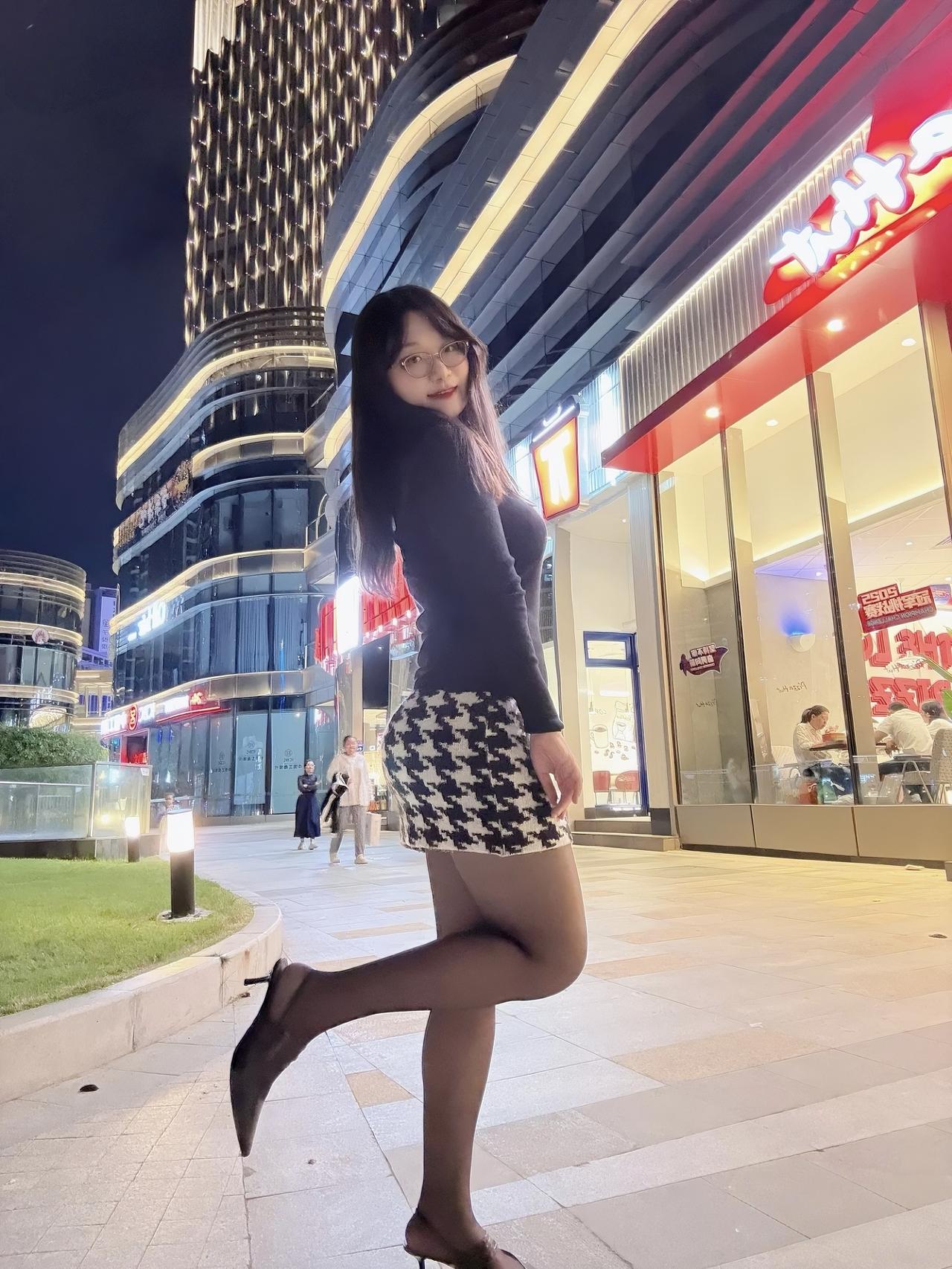 夜晚的商圈自带氛围感✨
黑针织+千鸟格短裙的组合，是轻熟风的小心机~
踩着细高跟