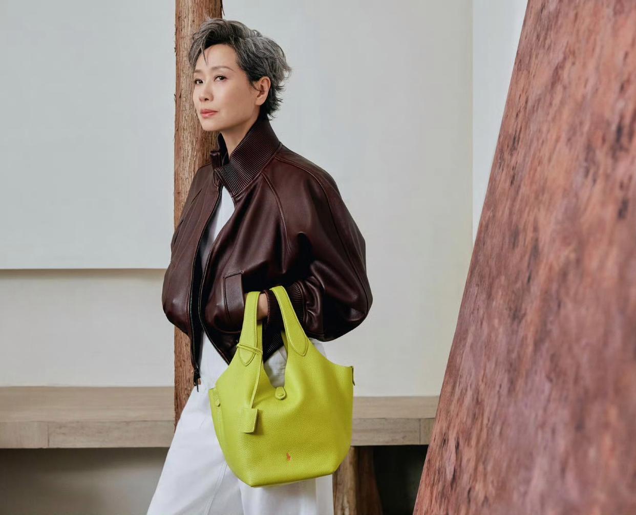 63岁叶童棕色皮衣穿搭分享：短款棕色皮衣搭配白裤，时尚酷感十足，手提黄绿色包包，