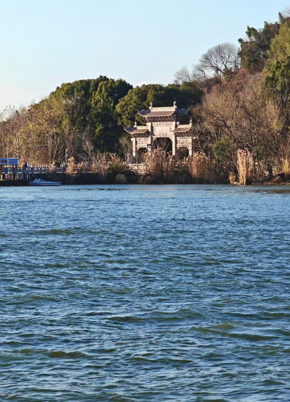 ✨蓝天下，湖水泛着绸缎般的光泽，远处的牌坊隐在树影里，仿佛尘世与山水私语的温柔标