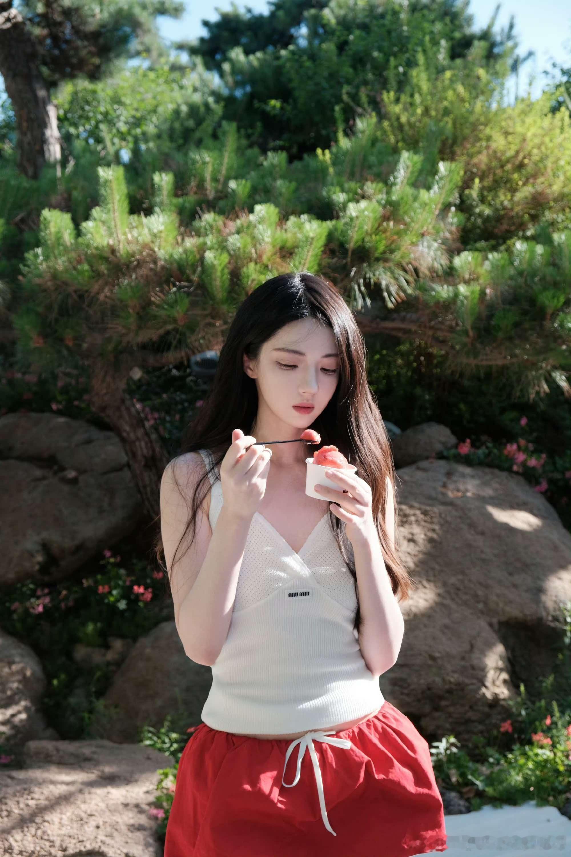 许荔莎阳光穿过松林碎落在肩头，白背心搭配红短裙清爽亮眼，手里一勺粉色冰沙衬得眉眼
