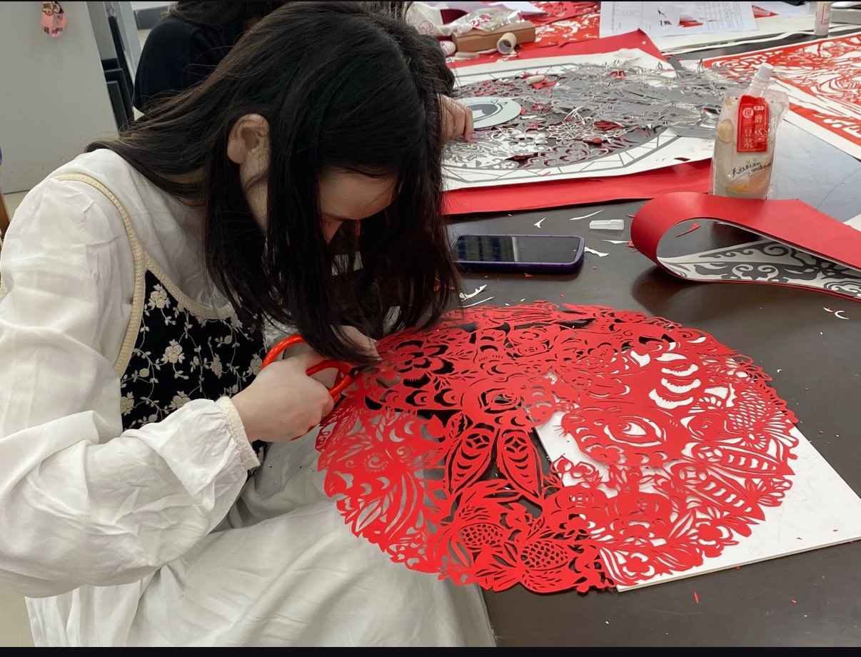 宿舍里的非遗细糠红纸在指尖翻折又铺开 剪刀咔嚓轻响 碎纸屑落满桌面 剪好的窗花贴