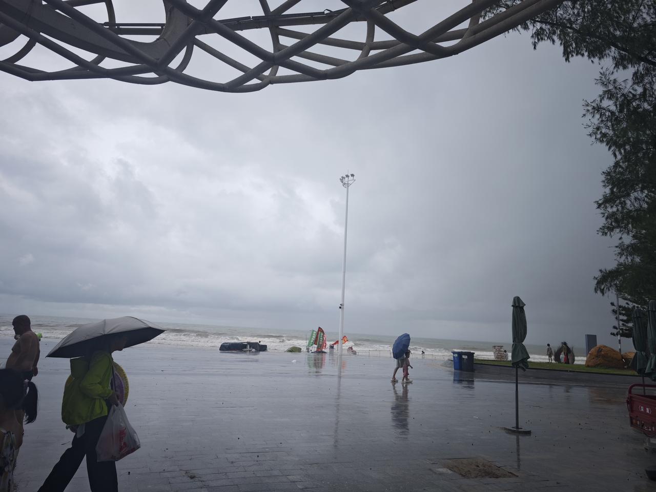 下雨天，海边的游客打着伞散步。