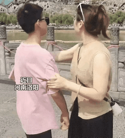 龙门石窟景区，妈妈拉儿子拍照打卡，儿子全程显酷，表示不情愿，妈妈的手比着“V”字