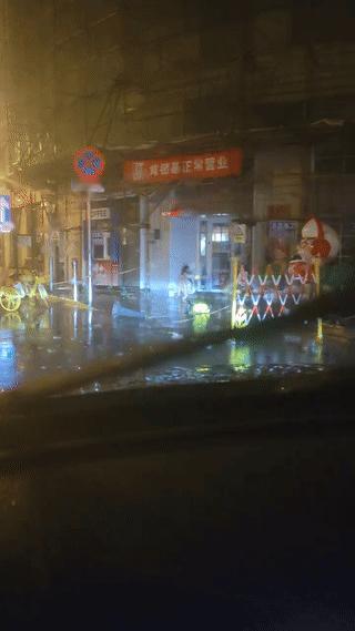凌晨的街头，天空中还下着小雨，网友拍到一名年轻女孩竟然独自一个人坐在一家临街店铺